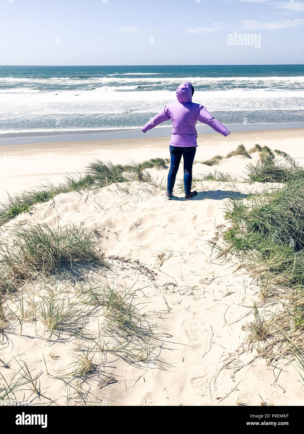 Woman standing on the beach with her arms outstretched in the wind, Florence, Oregon, America, USA Stock Photo
