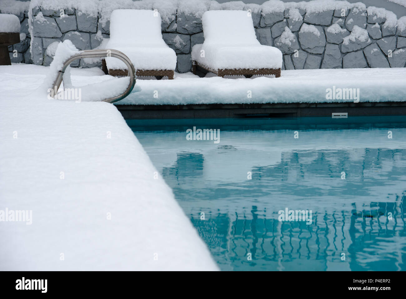 An outdoor swimming pool. the area around it and the lounging chairs covered in over half a foot, 20cm, of snow. Stock Photo