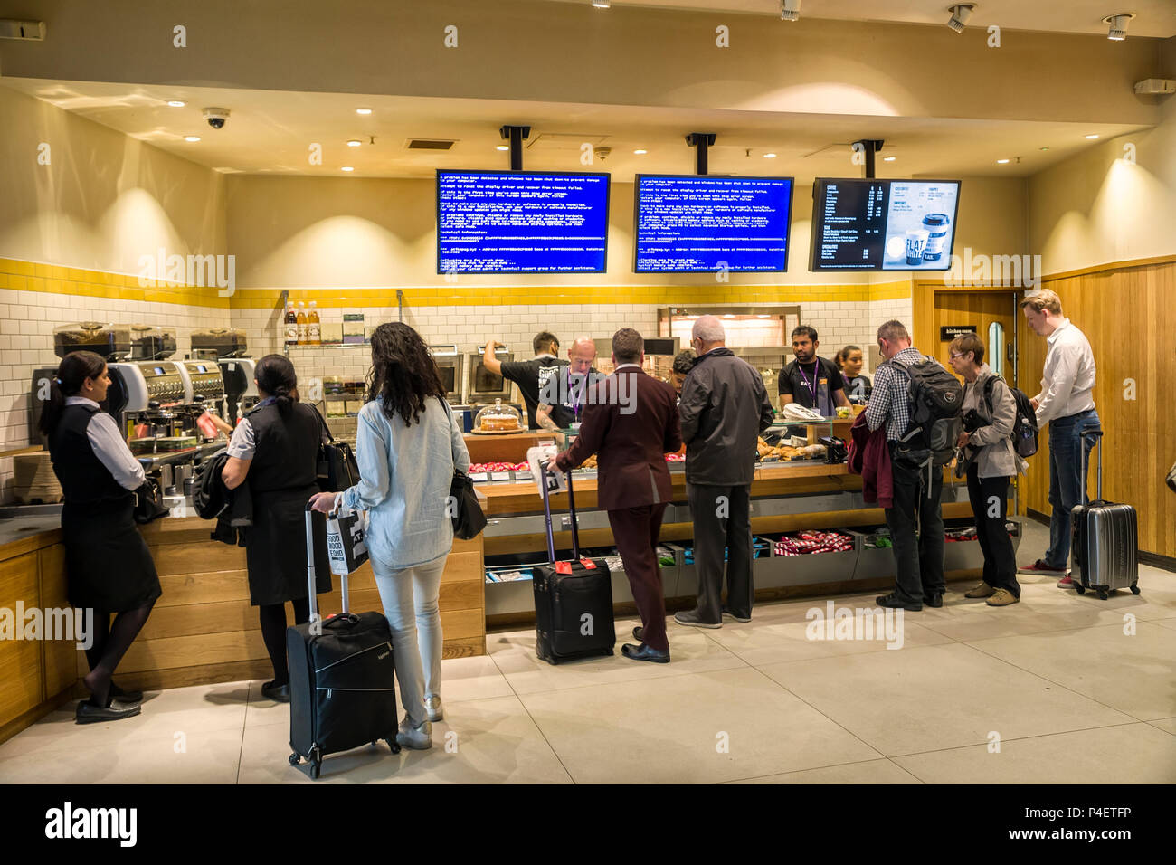 People buying fast food at counter with Windows blue screen on monitors, Heathrow, London airport, UK Stock Photo
