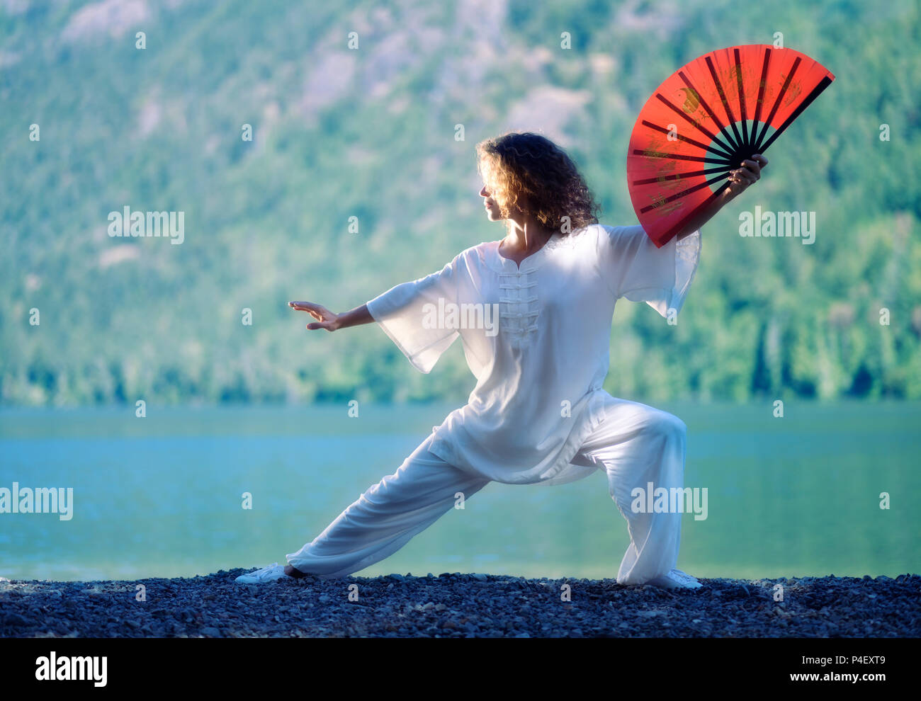 Young Woman Practicing Tai Chi Chuan With A Red Fan In The Morning Sunrise At A Mountain Lake Shore In The Nature Stock Photo Alamy