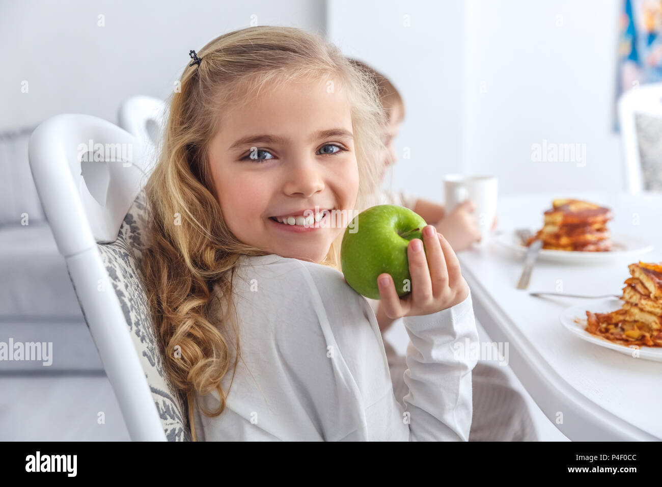 adorable little child with green apple looking at camera while having breakfast with family Stock Photo