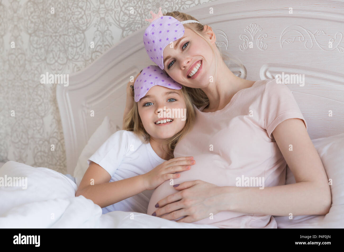 happy daughter and pregnant mother with eyes masks looking at camera
