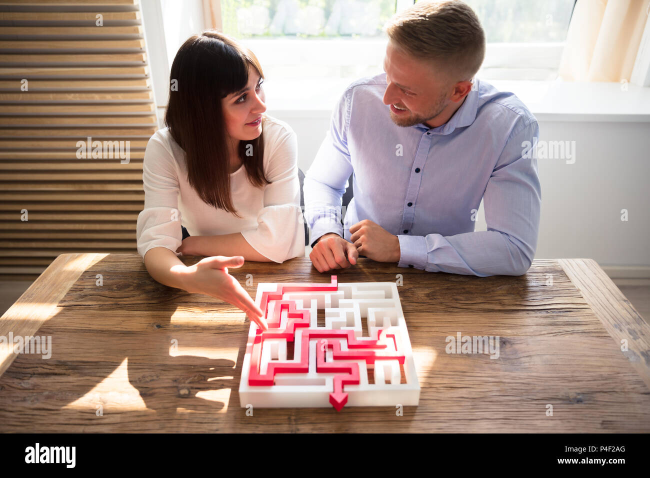 Two Young Businesspeople Solving Maze Puzzle Over Wooden Desk Stock Photo