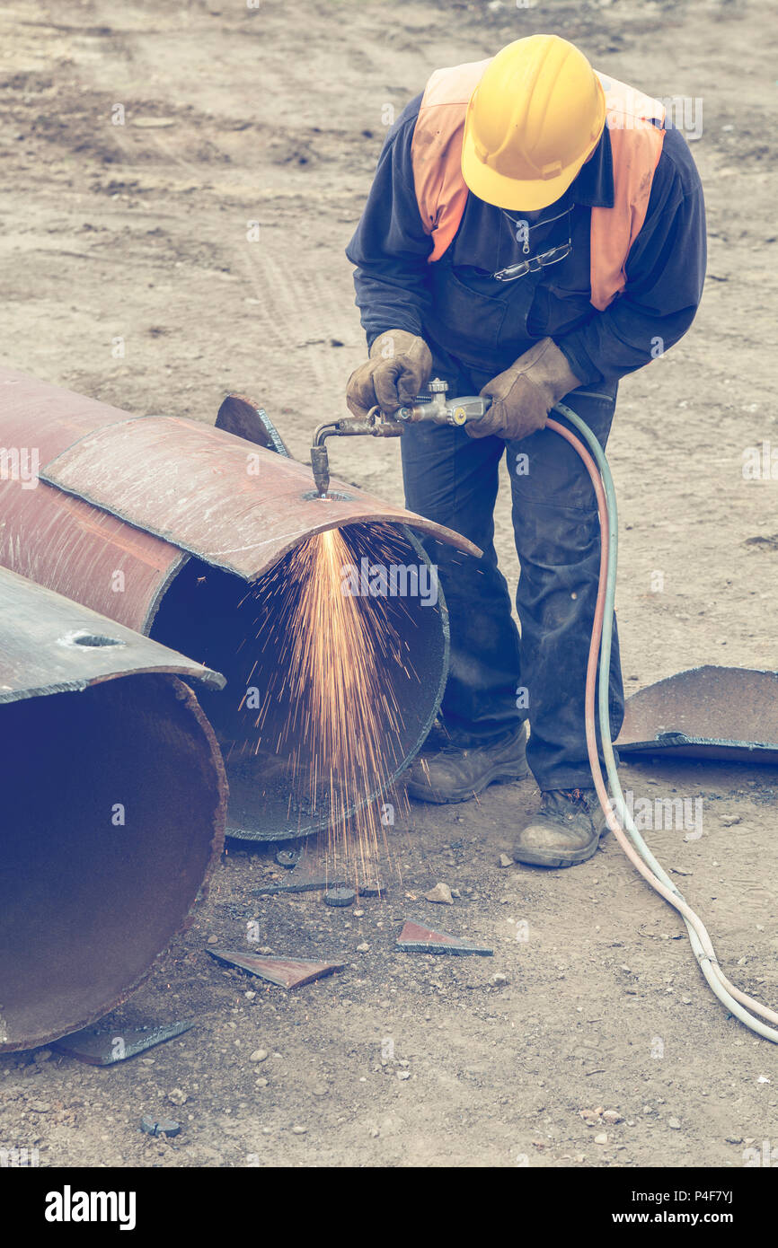 Welder worker with cutting torch, cutting hole in a steel pipe. Oxygen