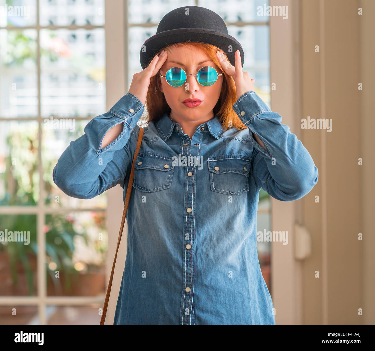 Stylish redhead woman wearing bowler hat and sunglasses with hand on