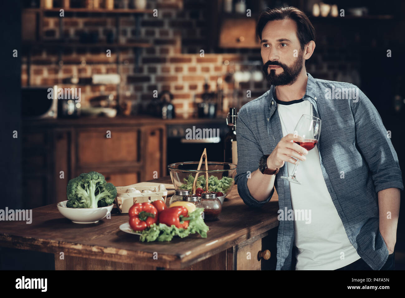 bearded mature man drinking wine while cooking dinner at home Stock