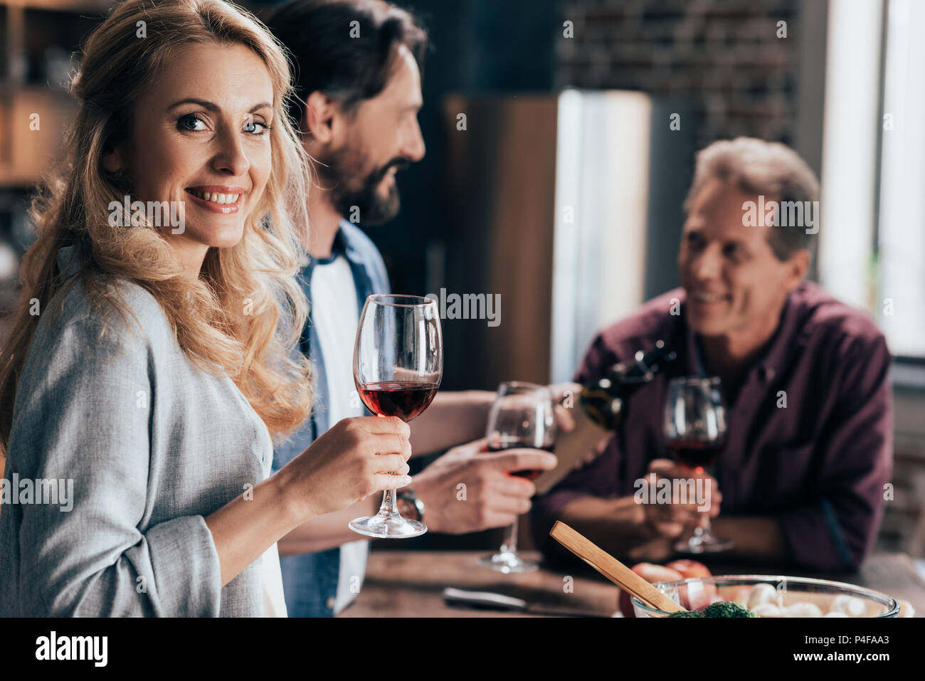 blonde woman with wine glass smiling at camera while drinking wine with ...
