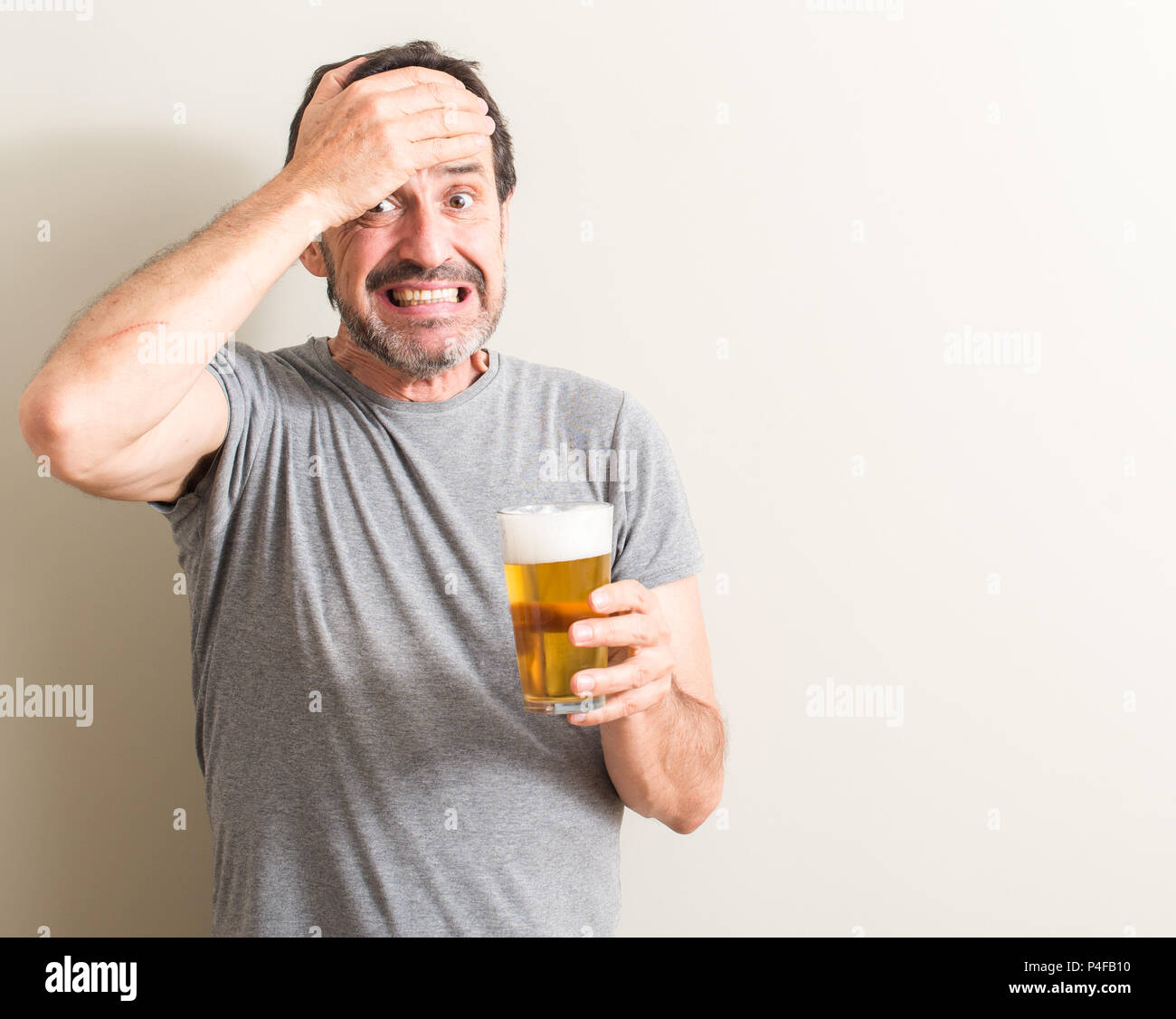 Senior man drinking beer stressed with hand on head, shocked with shame