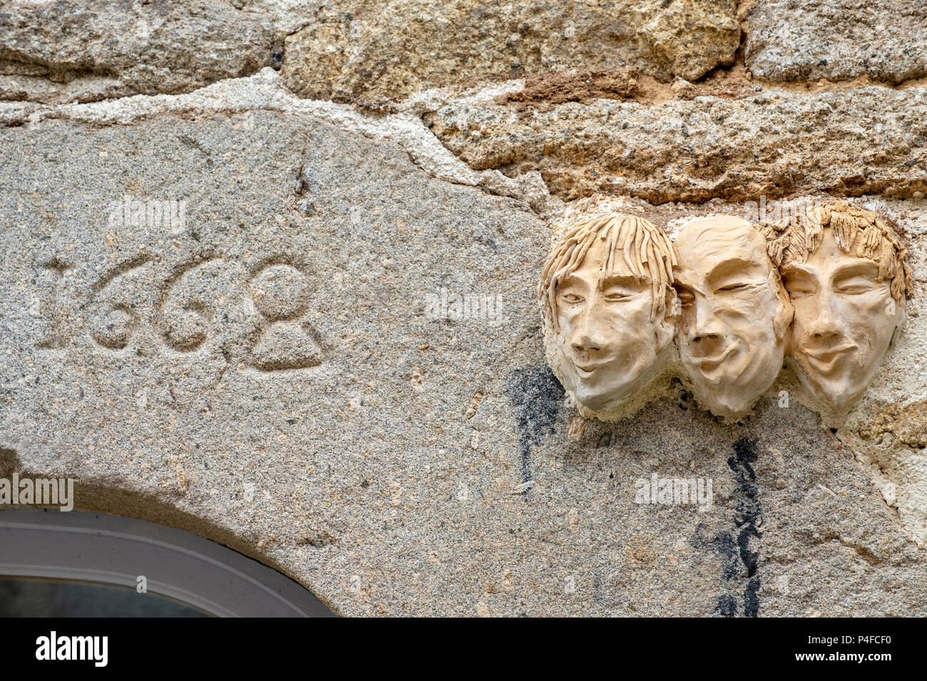 Clay faces sculpted on a wall above a doorway dated 1668 in Huelgoat, Brittany, France. Stock Photo