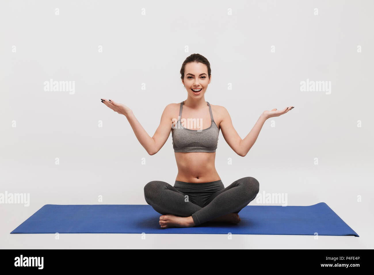 bewildered emotional young woman sitting on yoga mat isolated on white ...