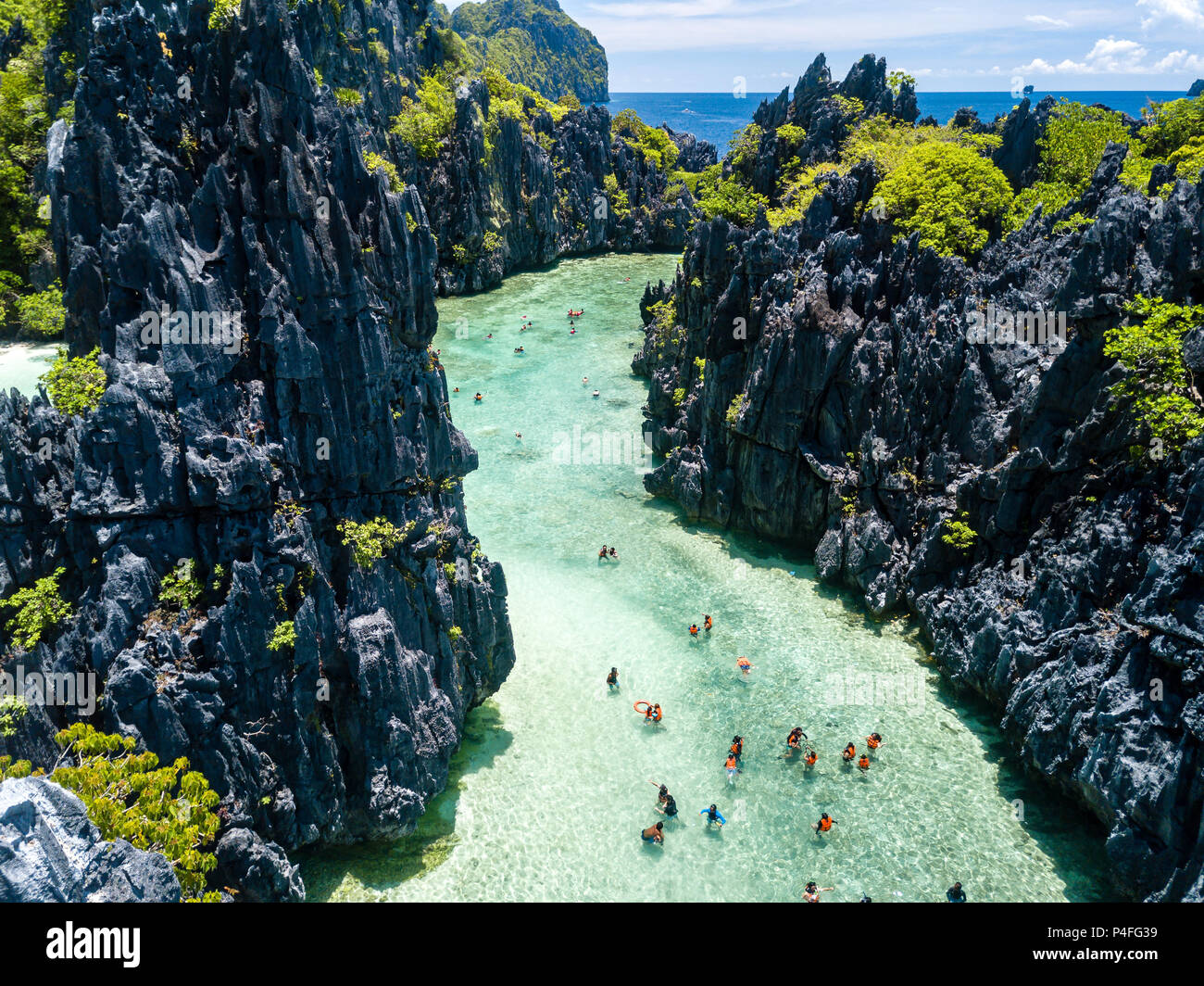 Aerial drone view of swimmers and tourists inside a beautiful, shallow tropical laggon surrounded by jagged cliffs Stock Photo