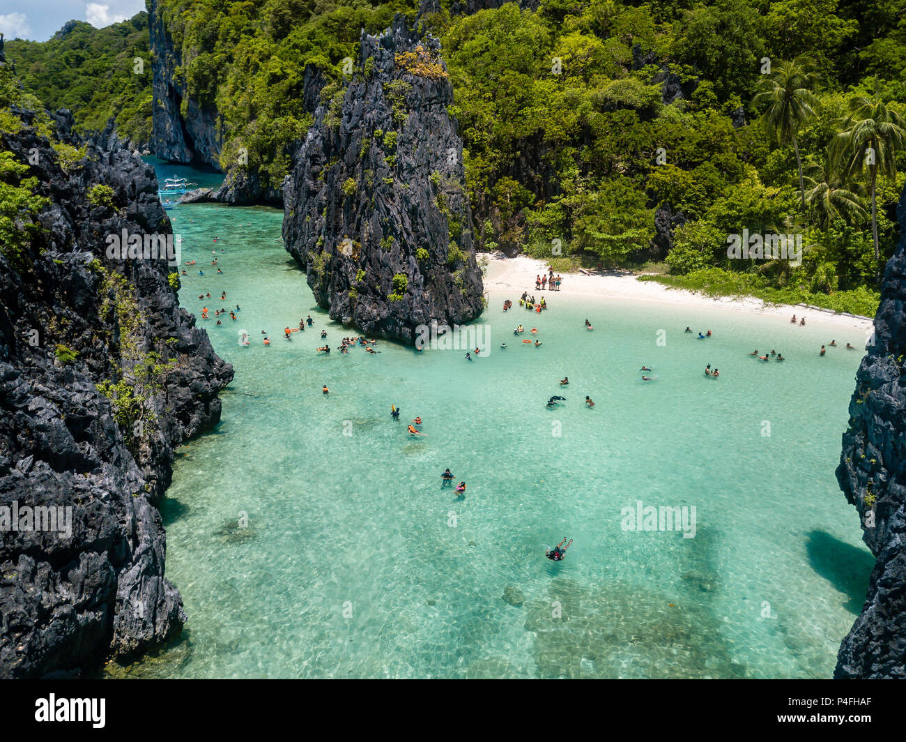 Aerial drone view of swimmers and tourists inside a beautiful, shallow tropical laggon surrounded by jagged cliffs Stock Photo