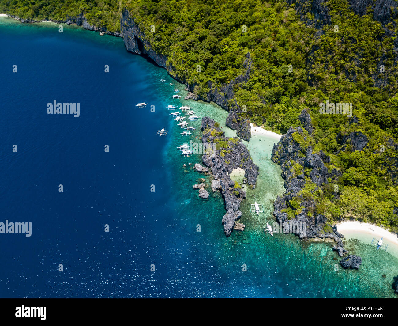 Aerial drone view of boats over a crystal clear coral reef and hidden sandy beach surrounded by cliffs (Hidden Beach, Palawan) Stock Photo