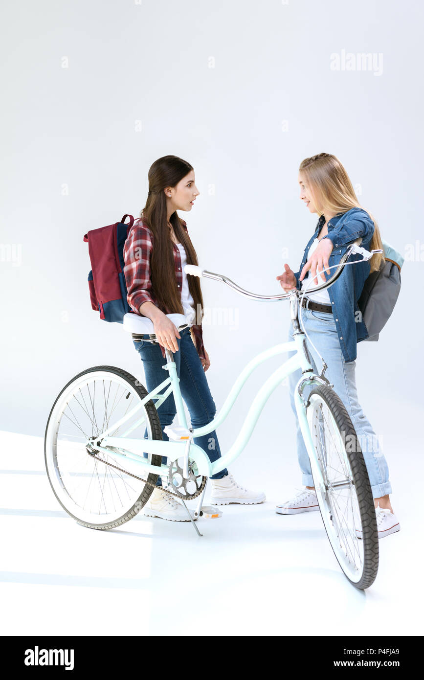 side view of teenage girls having conversation while standing near bicycle together isolated on white Stock Photo
