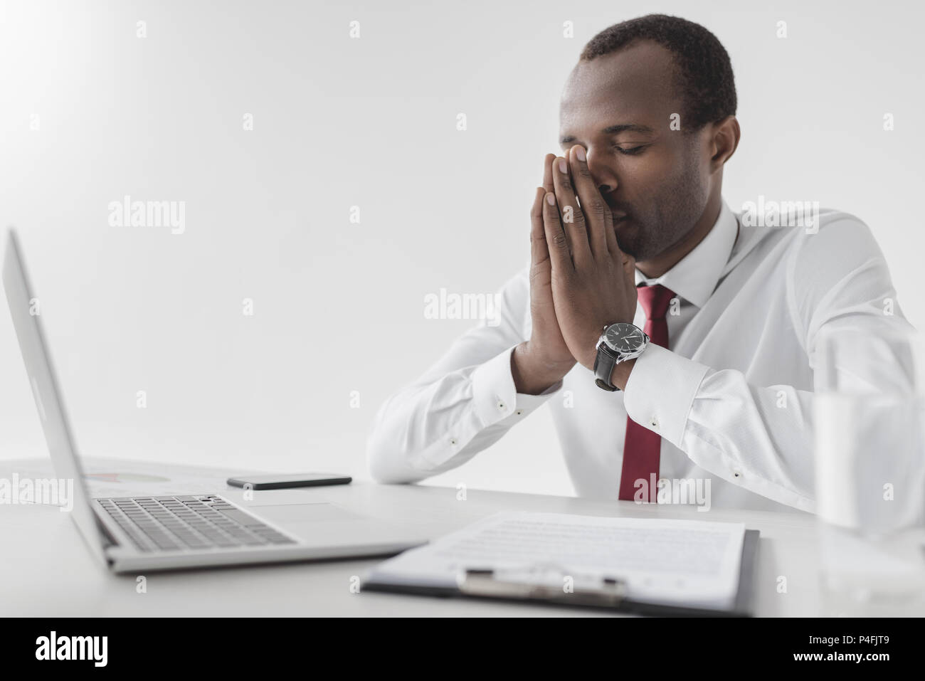 tired african american businessman sitting at workplace with laptop and document isolated on grey Stock Photo