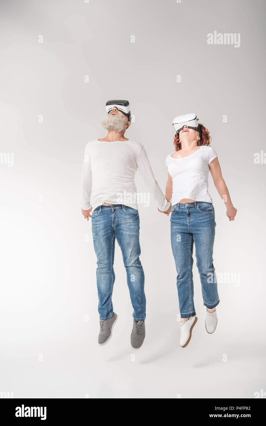 senior couple jumping while using virtual reality headsets, isolated on white Stock Photo