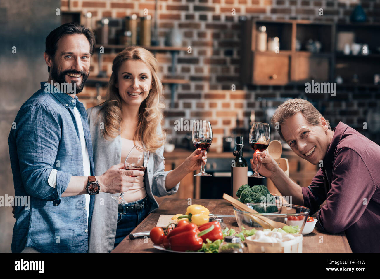 cheerful middle aged friends drinking wine while cooking dinner and