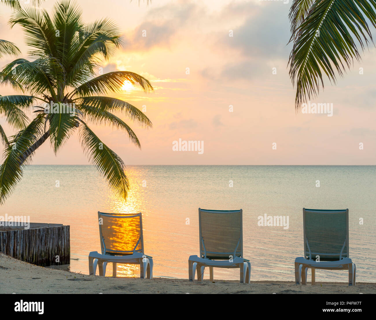 Sunrise over the ocean on dream beach vacation with palmtrees and deckchairs Stock Photo
