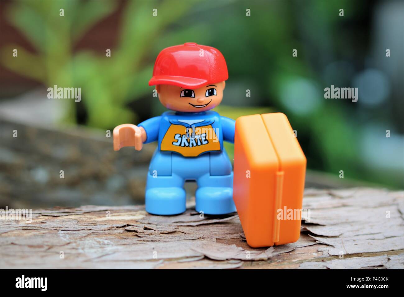 Duplo boy character holding a briefcase and wearing a red cap against a blurred background - News Concept Stock Photo