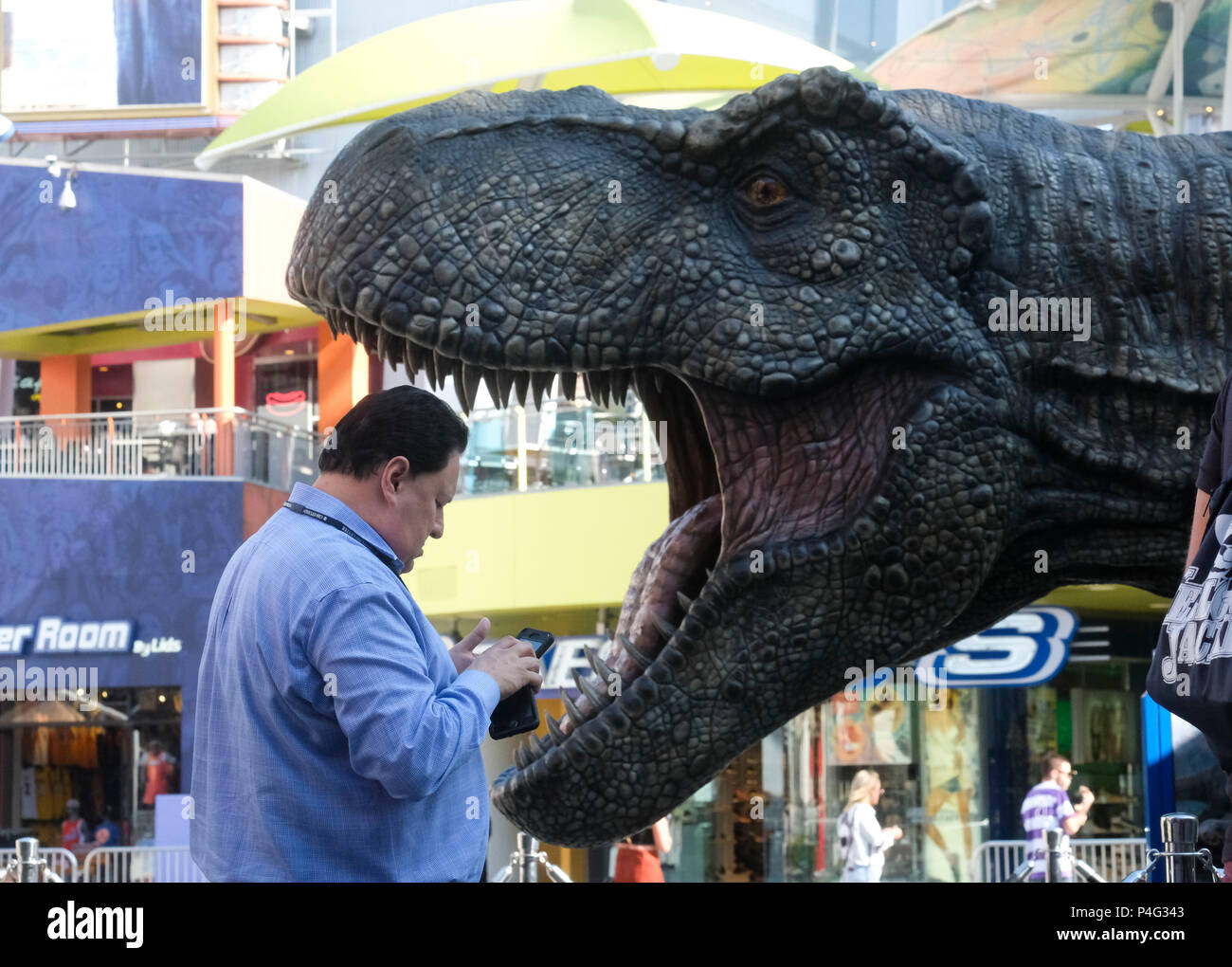 Los Angeles, USA. 21st June, 2018. A man passes by a giant Tyrannosaurus rex statue at Universal CityWalk in Los Angeles, the United States, on June 21, 2018. For the promotion of the screening of the new film 'Jurassic World: Fallen Kingdom' on Universal Cinema Theatres, a colossal 3-ton Tyrannosaurus rex, a life-sized Gyrosphere original movie prop, as well as original costume, are displayed for public at Universal CityWalk. Credit: Zhao Hanrong/Xinhua/Alamy Live News Stock Photo