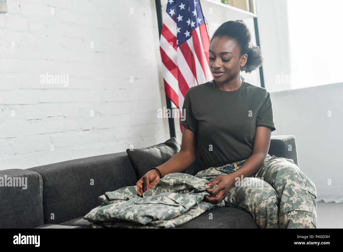 Female army soldier folding camouflage clothes on sofa Stock Photo