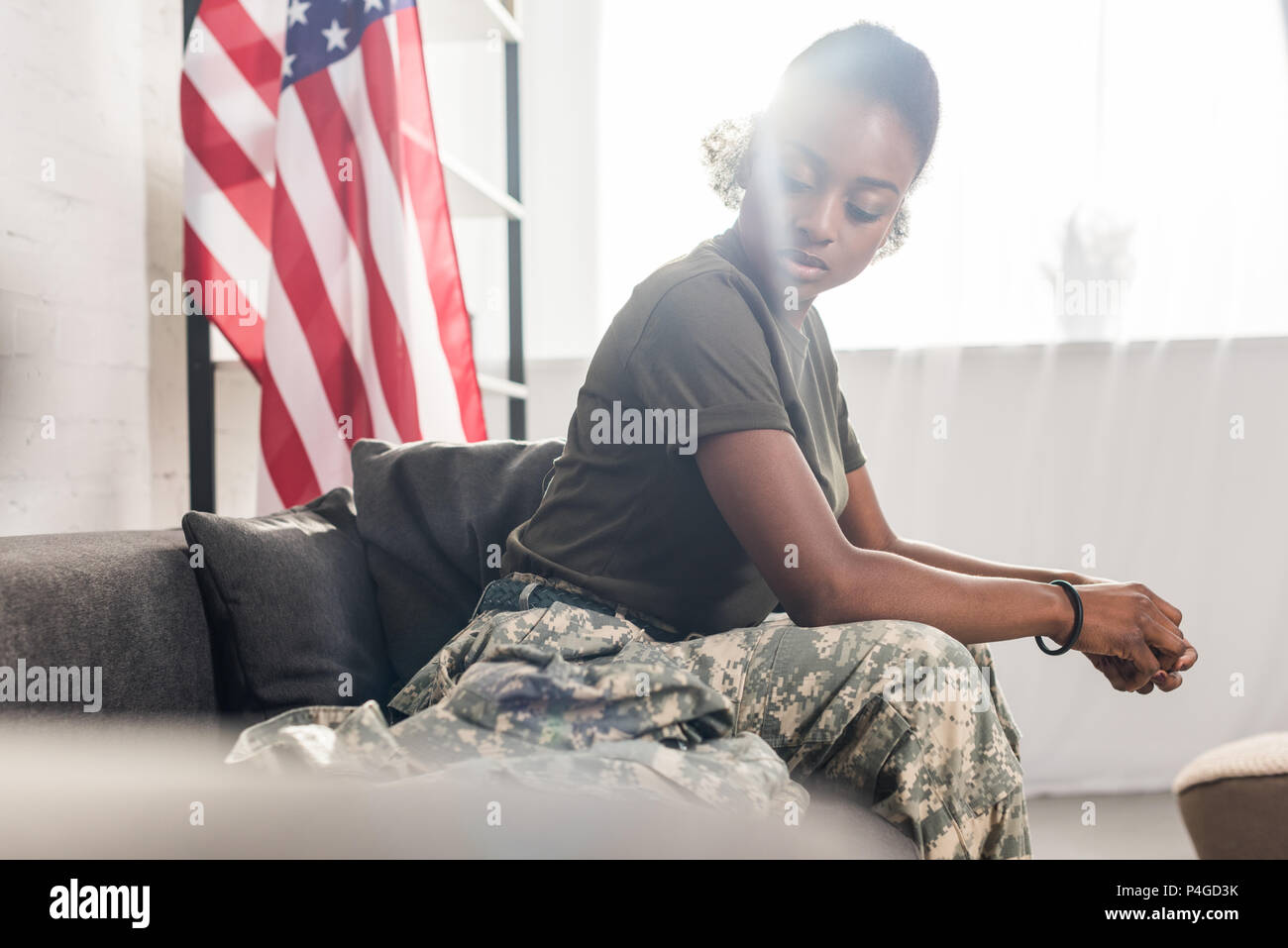 Female army soldier in camouflage clothes sitting on sofa Stock Photo