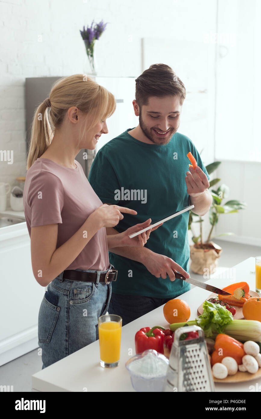 couple of vegans using tablet with recipe for preparing food at kitchen Stock Photo