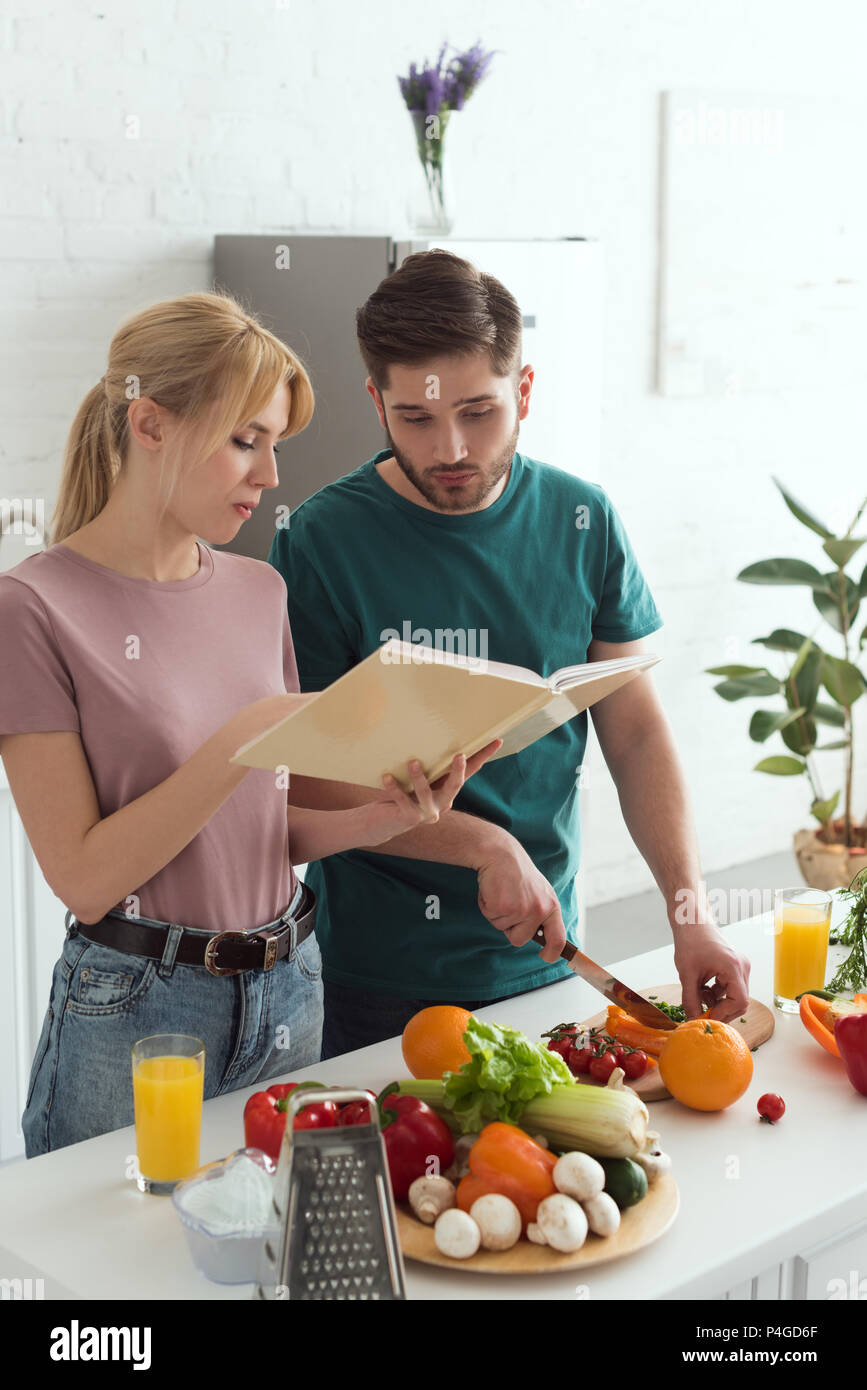 couple of vegans preparing food with cookbook at kitchen Stock Photo