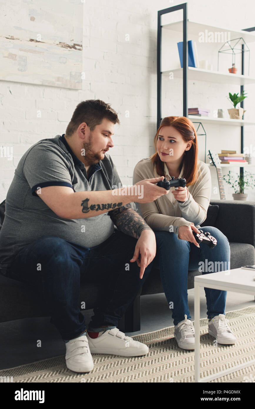 Girlfriend giving joystick to overweight boyfriend at home Stock Photo