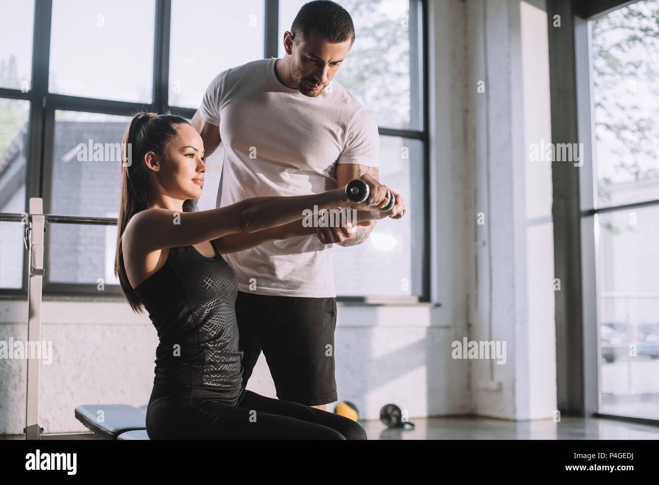 male personal trainer helping sportswoman to do exercises with ...