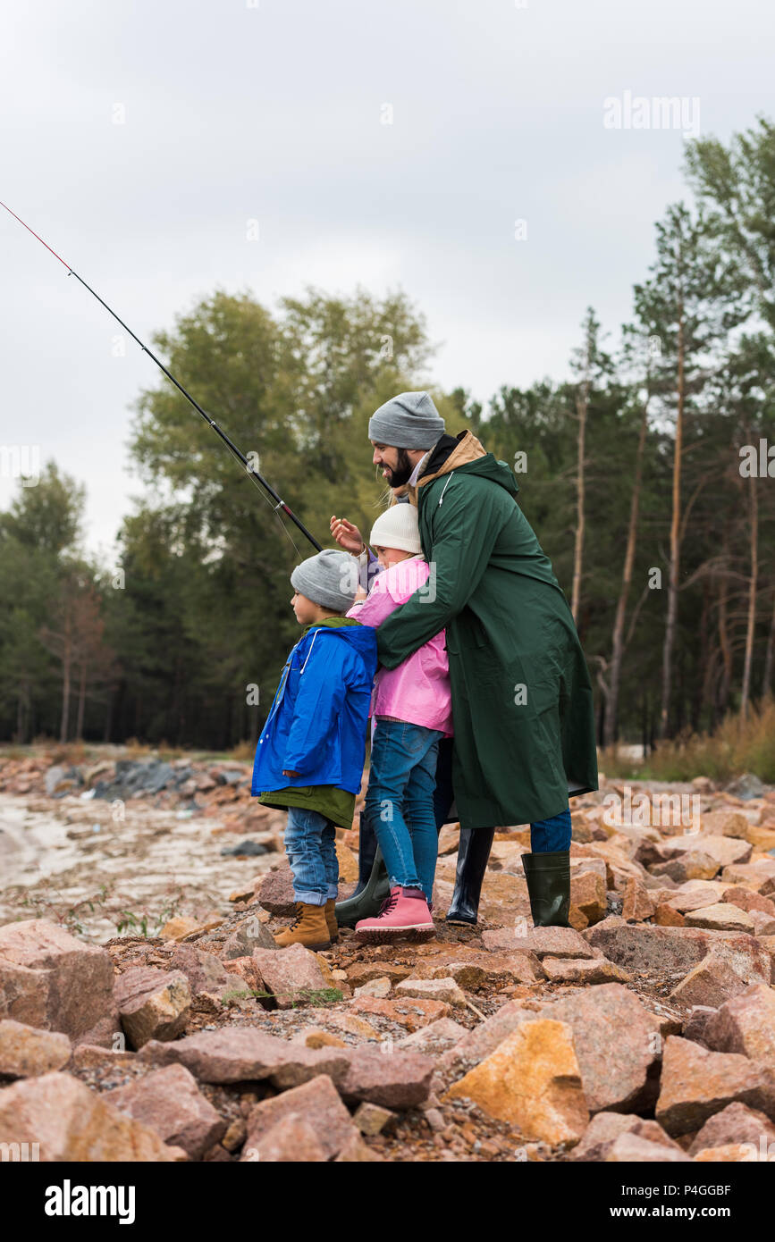 father and kids fishing together on rocky coast Stock Photo