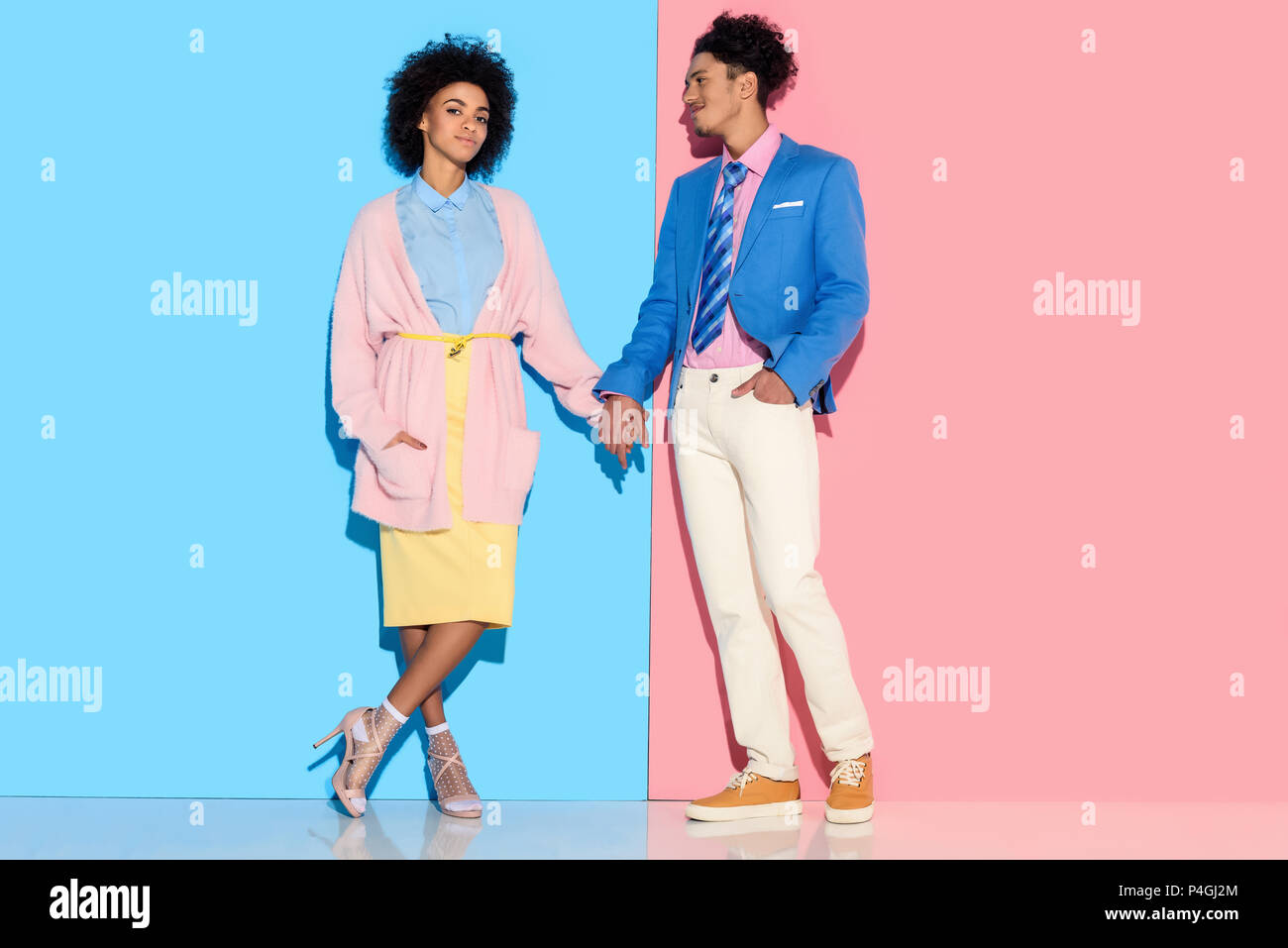 Young african amercian smiling girl and guy holding hands on pink and blue background Stock Photo