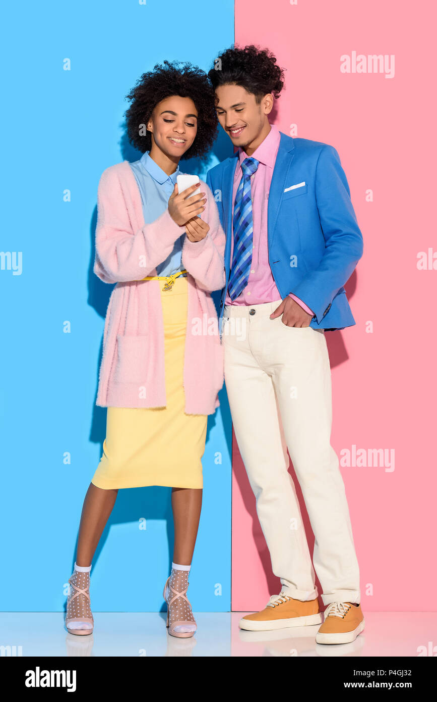 Young african amercian couple looking at phone screen on pink and blue background Stock Photo