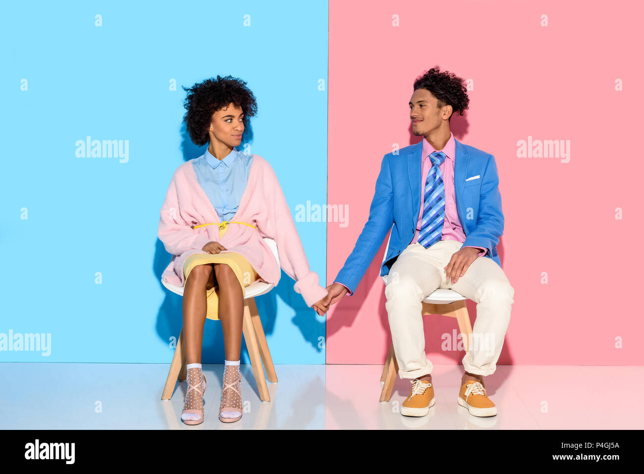 african american couple holding hands while sitting on chairs against ...