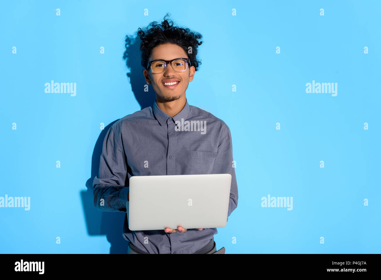 Young african amercian smiling man holding laptop on blue background Stock Photo