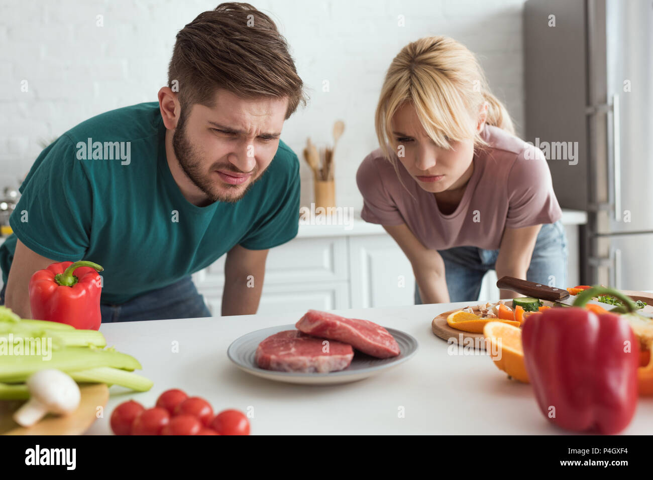 disgusted vegan couple looking at raw meat on plate in kitchen at home Stock Photo