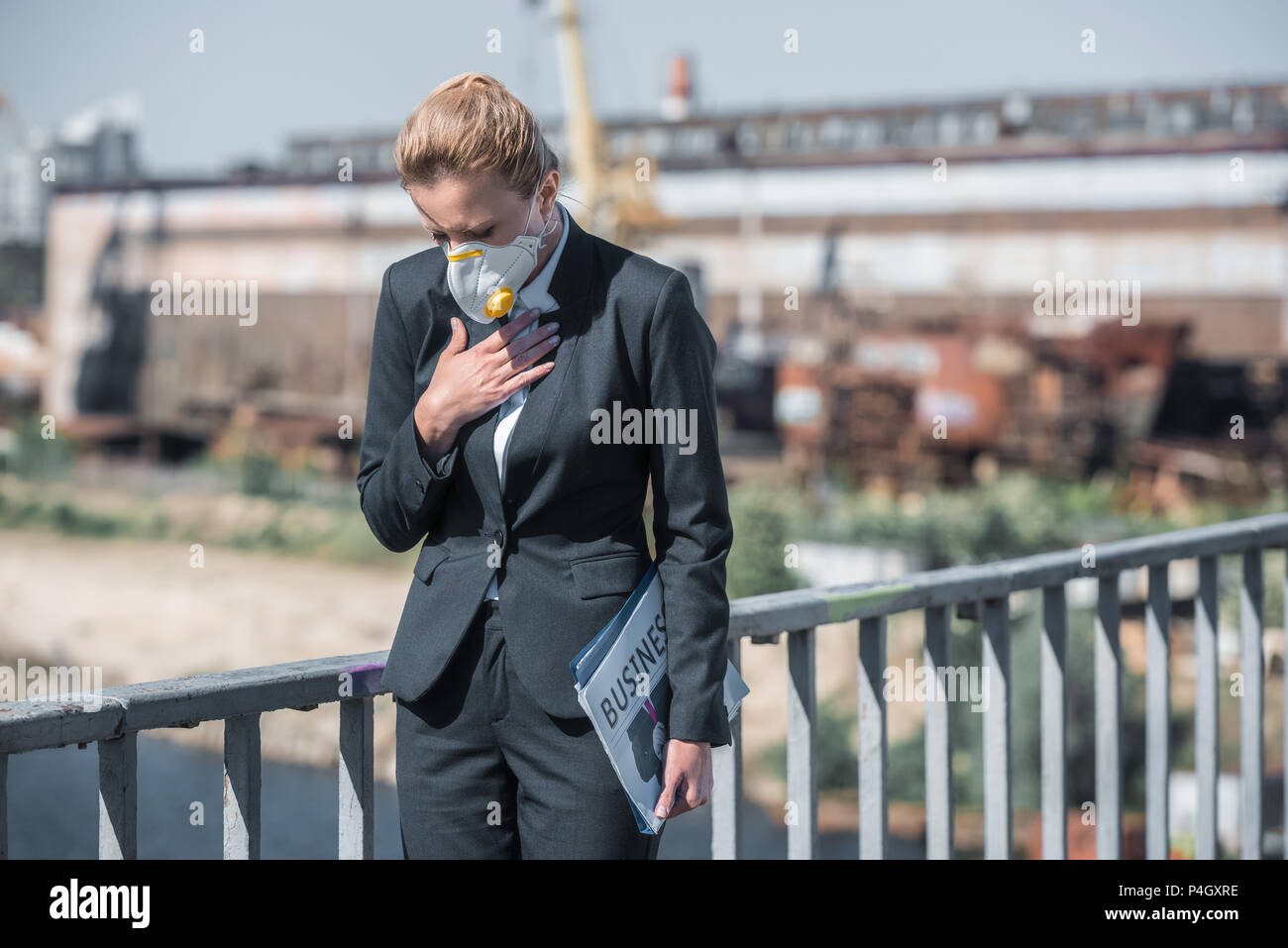 businesswoman in protective mask touching chest on bridge, air pollution concept Stock Photo