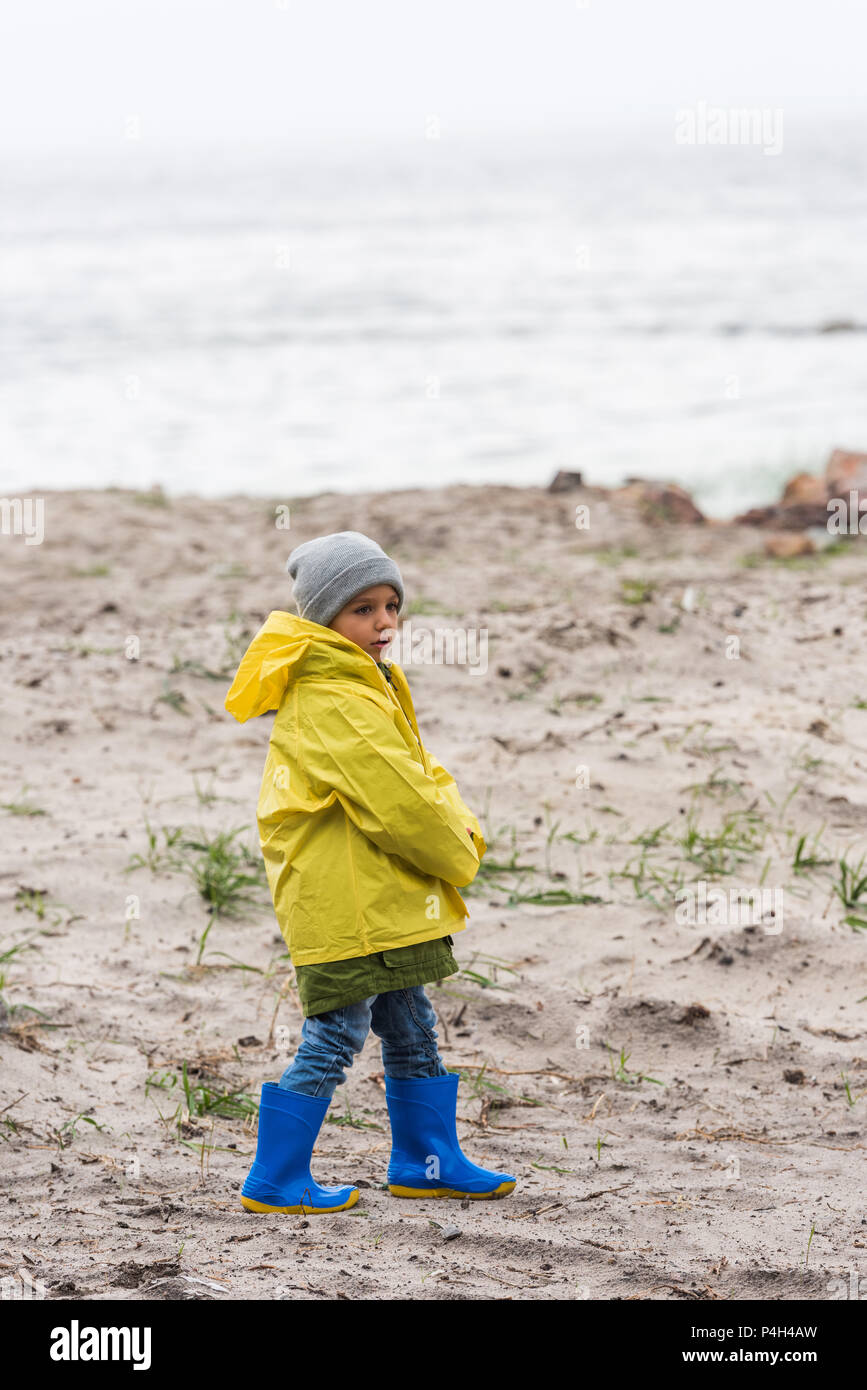 little boy in yellow raincoat and rubber boots on seahore Stock Photo