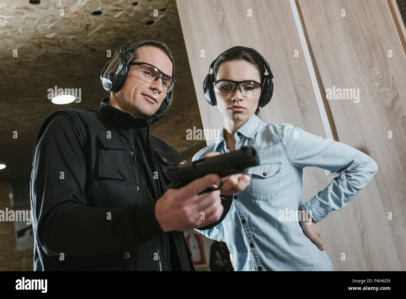 male instructor describing pistol to female client in shooting gallery Stock Photo