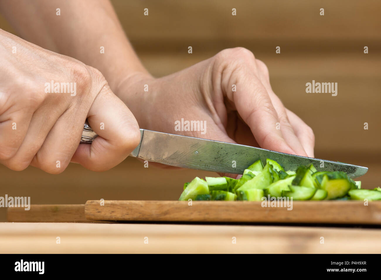 hands of woman slicing cucumber on the wooden cutting board Stock Photo