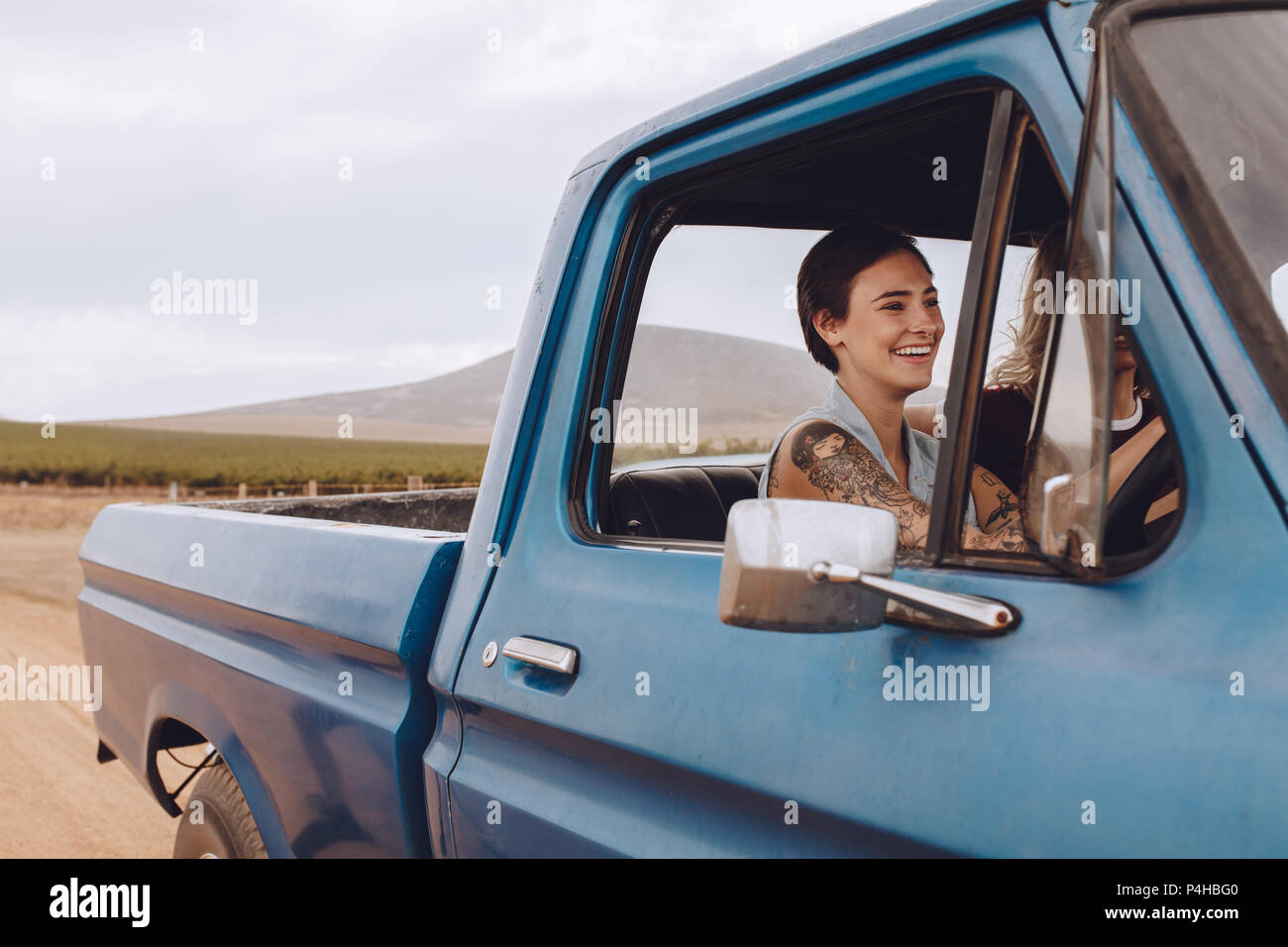 Smiling young woman driving a car on country road with female friend sitting next to her. Girls going on road trip. Stock Photo