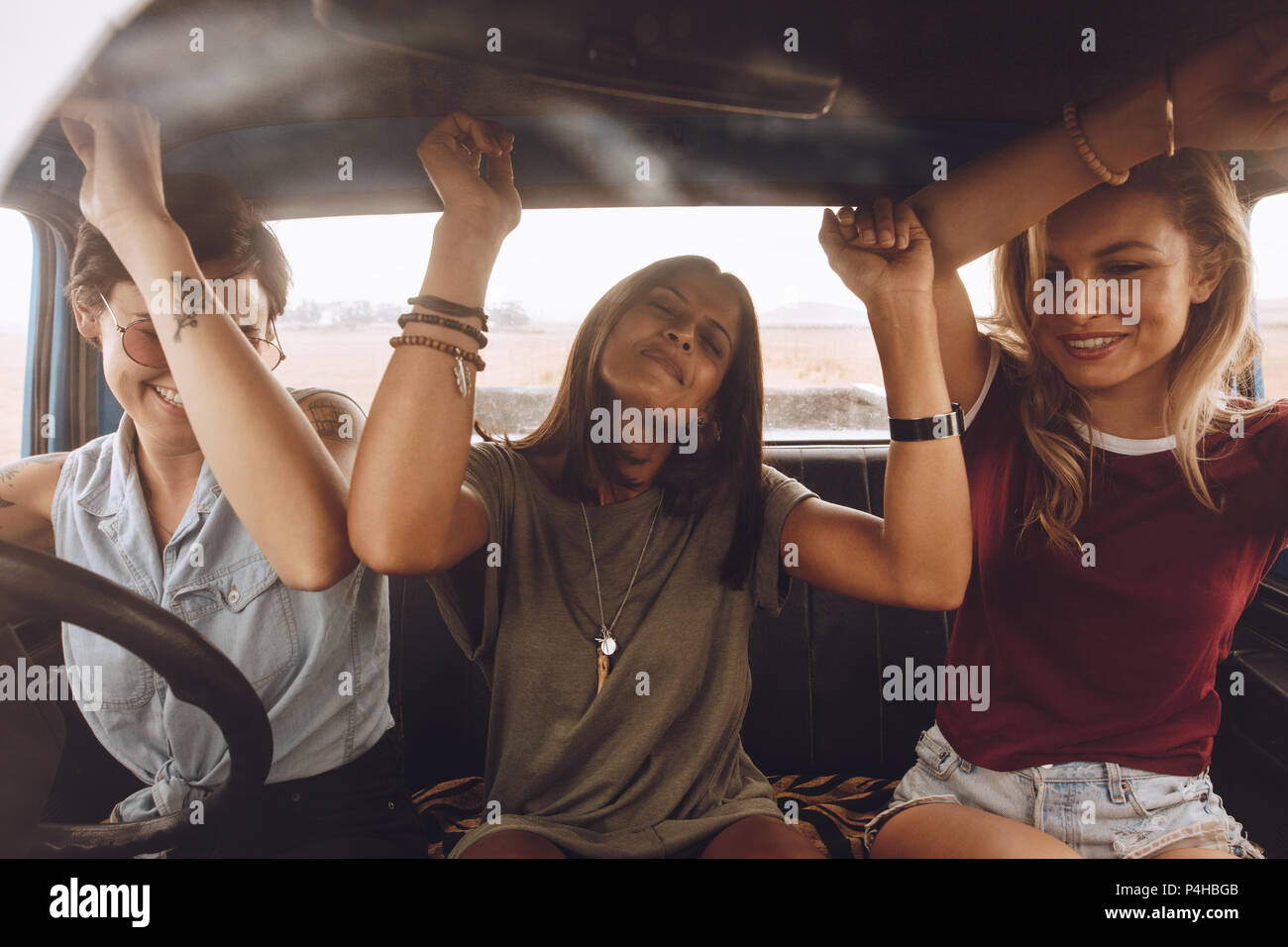 Three female friends enjoying traveling in the car. Women friends dancing in car during road trip. Stock Photo