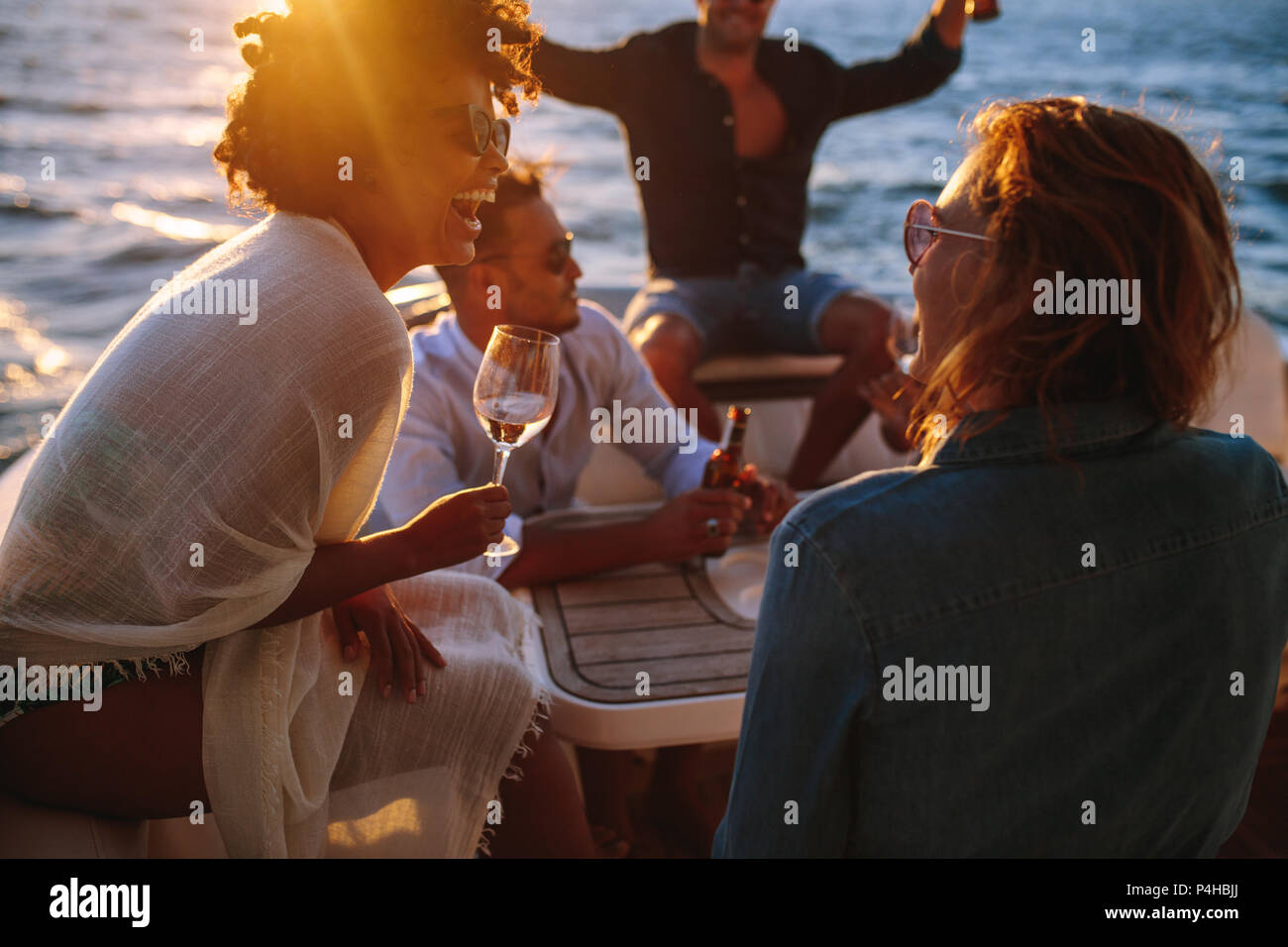 Cheerful young woman drinking wine while sitting with friends on a boat. Woman enjoying a boat party with friends. Stock Photo
