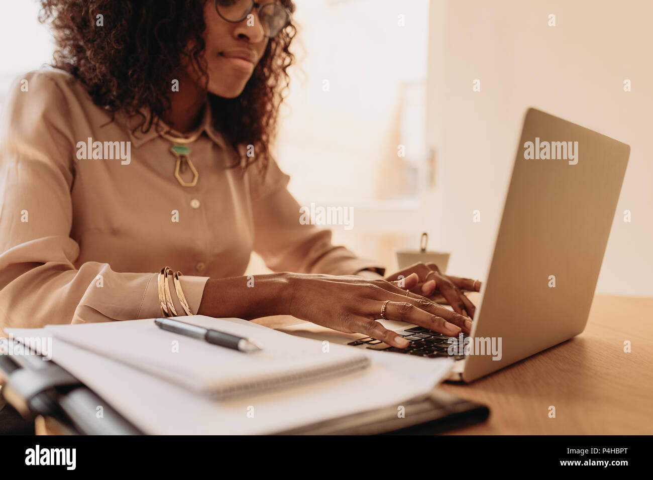 Businesswoman working on laptop computer from home. Woman entrepreneur sitting at home working on laptop with business documents on the table. Stock Photo