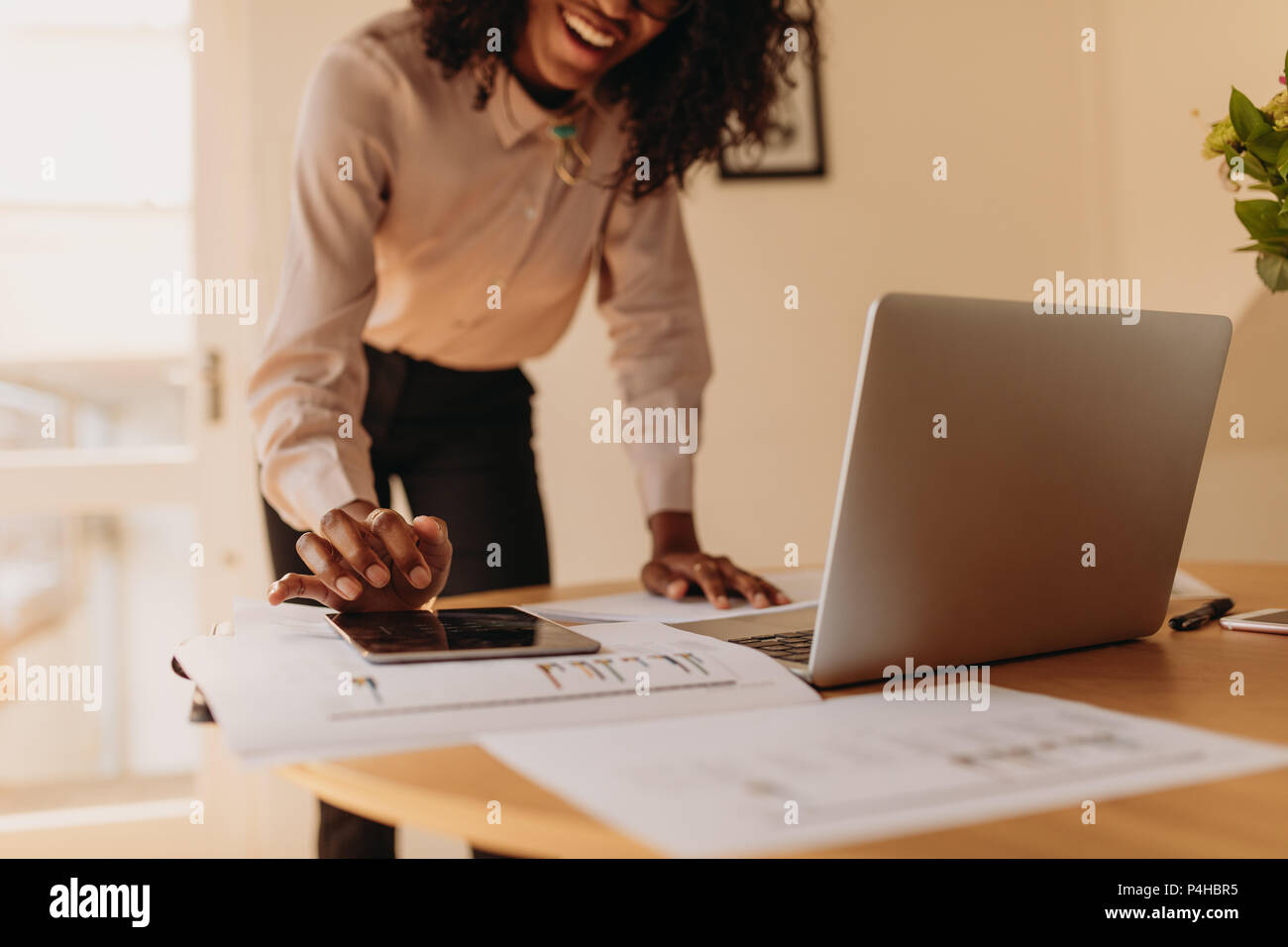 Businesswoman using a tablet pc while working on laptop computer at home. Woman entrepreneur standing beside the table using tablet pc while working o Stock Photo