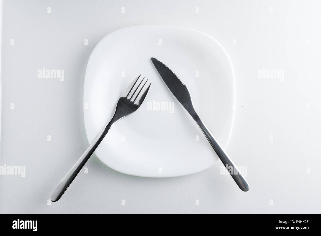 fork and knife on an empty white plate on a white background top view ...