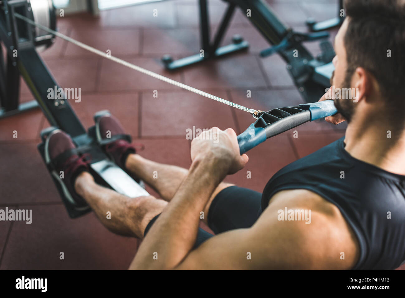 Cropped image of young sportsman doing exercise on rowing machine in sports center Stock Photo