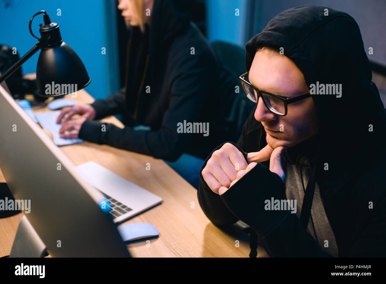 thoughtful young hacker looking at computer screen in dark room Stock Photo