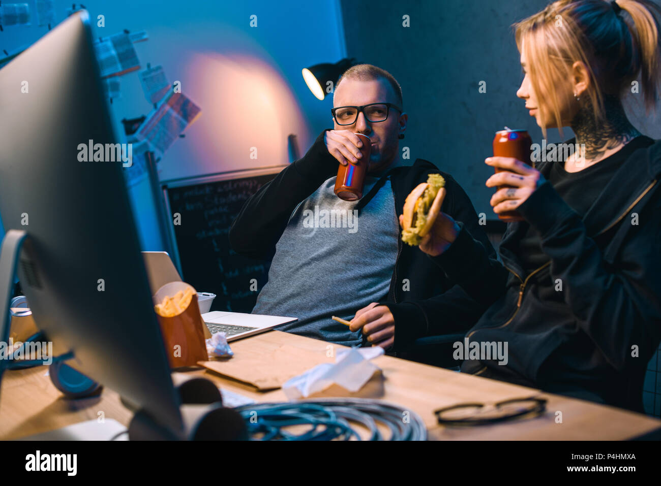 young hackers drinking beer and eating junk food while working on malware Stock Photo