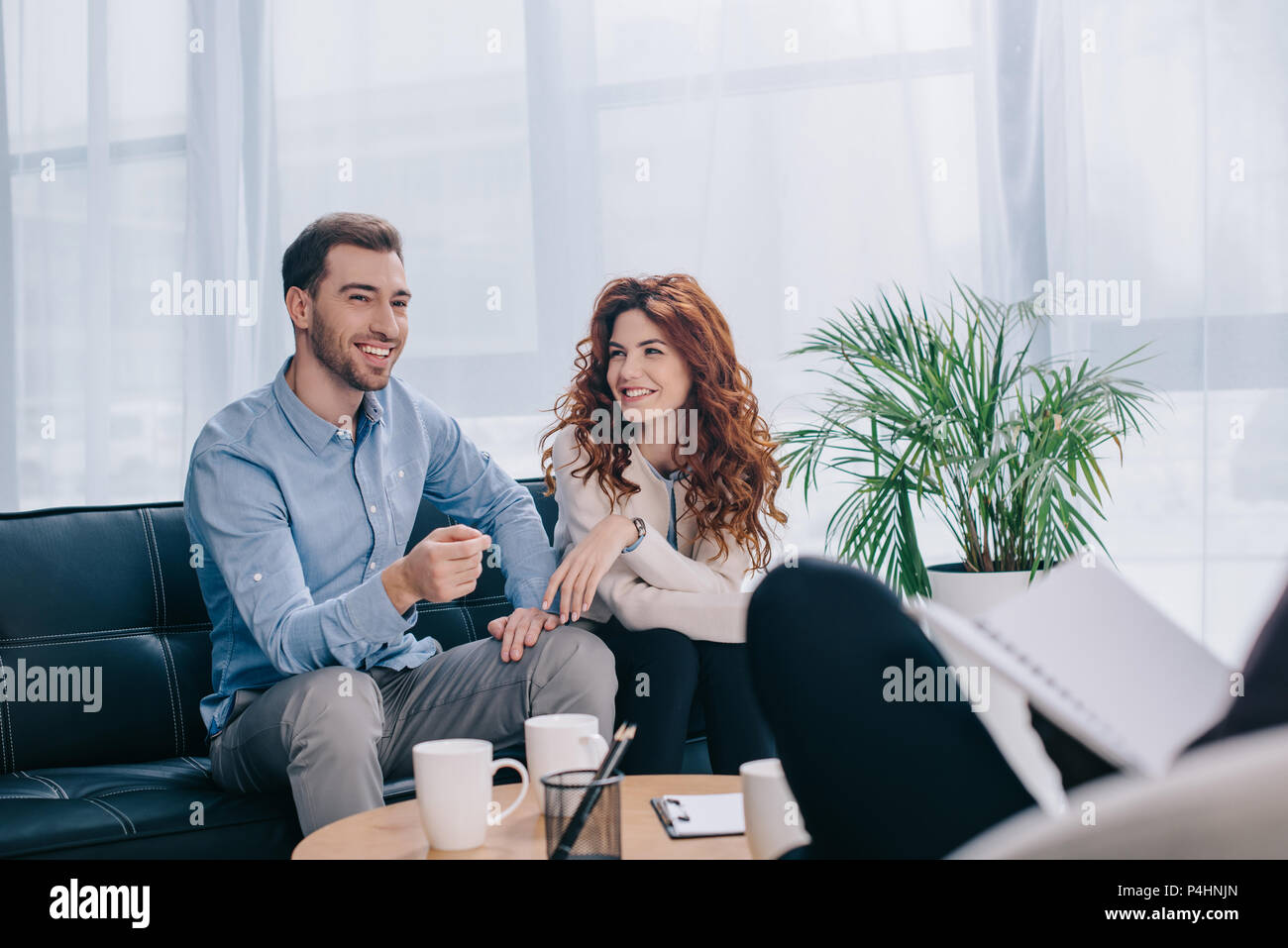 Smiling young couple sitting on sofa in counselor office Stock Photo